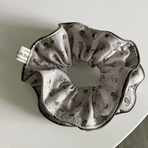 Detailed view of grey floral scrunchie featuring vintage patterns and a premium brand label