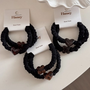 Detail of black pleated fabric hair ties with amber acrylic heart and flower charms