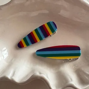 Close-up of rainbow striped acrylic hair clips on a white ceramic tray with metallic base
