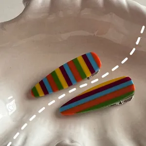 Detail view of rainbow striped duckbill hair clips on white shell tray with random patterns