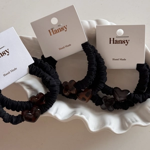 Detail of black fabric hair scrunchies with amber heart and flower charms on card
