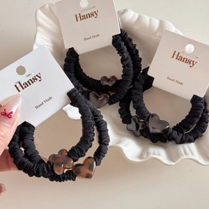Close-up of leopard print heart charms on pleated black elastic scrunchies on a shell tray