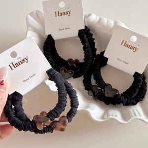 Close-up of black scrunchies with leopard heart and clover charms in a ceramic shell dish