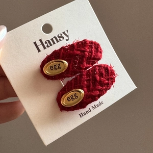 Detailansicht von zwei handgefertigten roten Tweed-Haarspangen mit goldenem Metallemblem