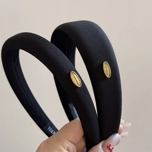 Close-up of black padded fabric headband featuring a gold metal brand tag detail
