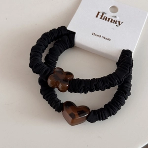Detail of two black scrunchies featuring heart and clover tortoiseshell charms on card