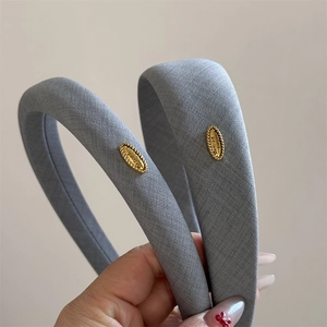 Detail of grey fabric headband featuring a gold metal tag with Refined Elegance engraving