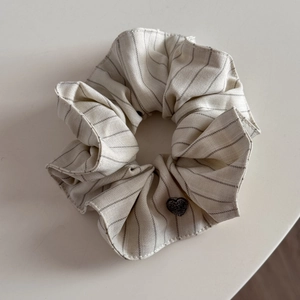 Detail of grey striped fabric scrunchie with dark heart-shaped accent on beige background