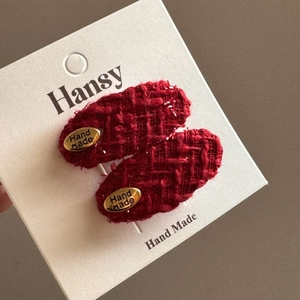 Detail von roten Tweed-Haarspangen mit goldenen Anhängern auf weißer Displaykarte