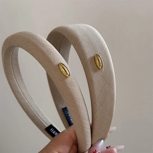 Detailed macro view of beige fabric headband with gold metal tag and thick padding