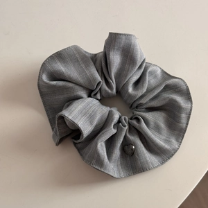 Close-up of grey striped scrunchie with detailed heart pendant and pleated fabric texture