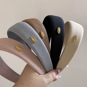 Detail of five wide fabric headbands in assorted colors with elegant gold metal tags