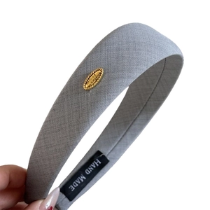 Gray fabric wide headband with textured twill finish and gold metal label detail