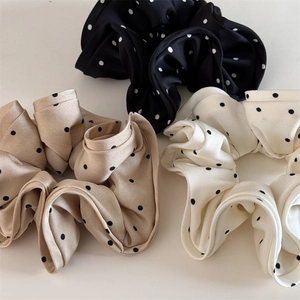Close-up of three satin polka dot scrunchies in black, champagne and ivory white