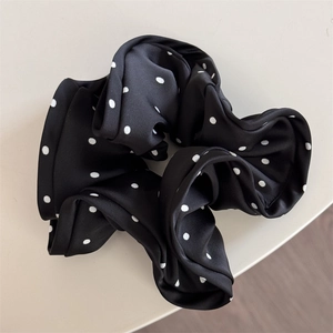 Detailed close-up of a black satin scrunchie with white polka dots on a plain desk
