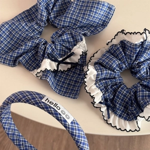 Close-up of blue plaid scrunchie with white ruffled edges and a navy bow hair accessory
