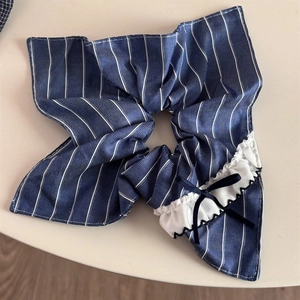 Detailed close-up of blue striped fabric scrunchie with white ruffle and black bow accent