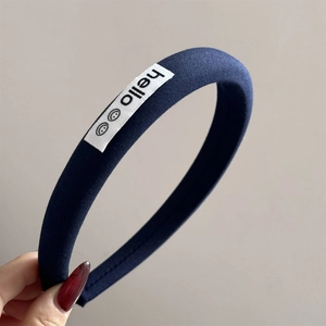 Detail of navy blue fabric headband with white square label showing smile face and hello text