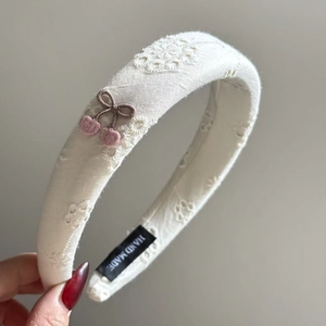 Detail of handmade hollow floral embroidery with pink cherry accent on beige headband