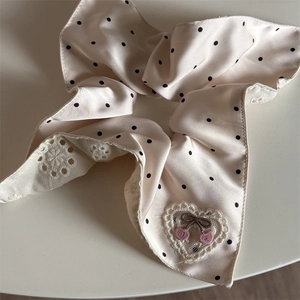 Detailed embroidery of small cherries and a bow on a white polka dot lace hair scrunchie
