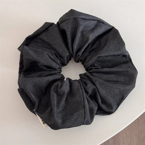 Détail d'un chouchou en denim noir foncé avec plis souples et texture tissée apparente