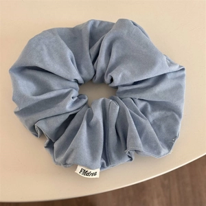 Gros plan sur un chouchou en denim bleu clair avec texture tissée et étiquette en tissu blanc
