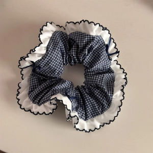 Detailed shot of blue gingham scrunchie with white ruffle edges and small bow accents