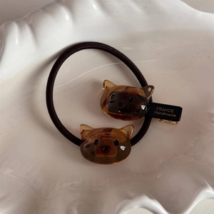 Détail de l'élastique chat en acétate ambre et pince à cheveux dorée dans un plat céramique