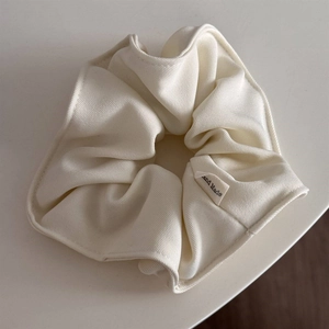 Detailed macro view of cream-white twill fabric scrunchie with Hand Made woven label