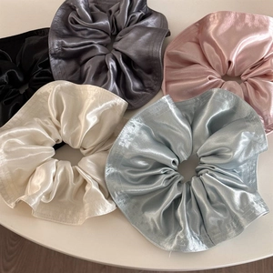 Five oversized satin scrunchies in black, grey, pink, cream, and blue with high sheen