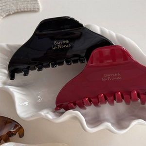 Détail de pinces à cheveux en acétate noir et bordeaux avec logo doré sur plateau