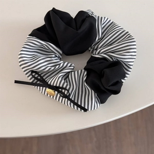 Detail of black and white striped scrunchie with silk ribbon bow and gold logo charm