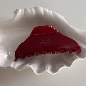 Détail de la pince à cheveux rouge en acétate avec texte doré sur un plateau coquillage