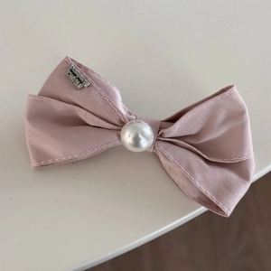 Detail of pink satin bow hair clip with faux pearl and engraved handmade metal tag