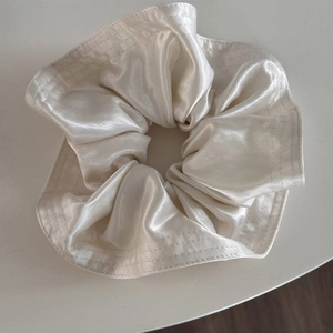 Detailed close-up of champagne satin fabric texture with triple stitched edge on hair scrunchie