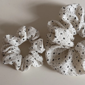 Detail von weißen Blumen-Haargummis aus plissiertem Stoff mit schwarzem Muster