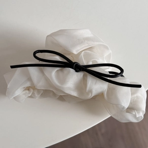 Détail d'un chouchou élégant en organza crème avec un petit nœud papillon noir