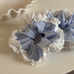 Détail de deux chouchous à rayures bleues avec bords en dentelle blanche sur fond crème