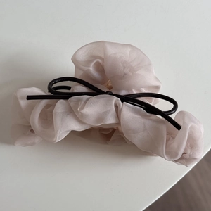 Détail d'un chouchou en organza rose clair plissé avec un petit nœud noir élégant
