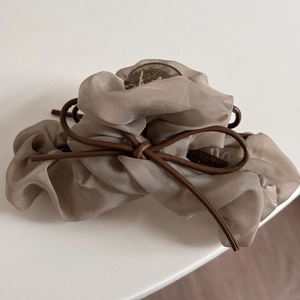 Détail de la pince à cheveux en organza beige avec un nœud en cuir marron foncé