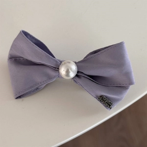 Detailed macro view of a purple lace bow hair tie with a pearl center and handmade metal tag