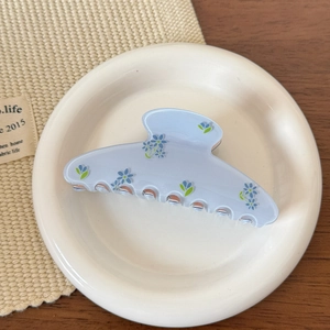 Gros plan d'une grande pince à cheveux bleue mate avec motif floral sur assiette blanche