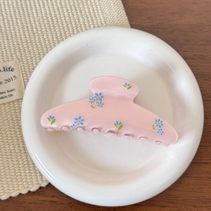 Détail d'une pince à cheveux rose clair à fleurs bleues sur une assiette blanche