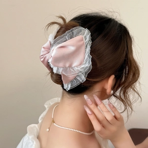 Detailed back view of model wearing a pink satin bow hair claw with white lace trim