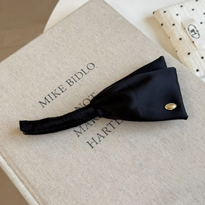 Detail shot of black satin banana clip showing fine pleated fabric and gold metal plate