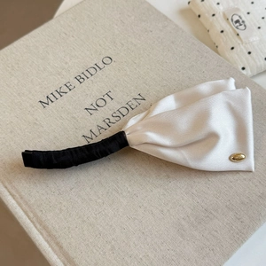 Detail of satin ribbon banana clip with cream bow and golden logo on fabric background