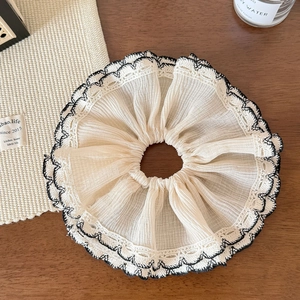 Détail d'un chouchou en dentelle crème avec bords noirs ondulés et texture de tissu plissé