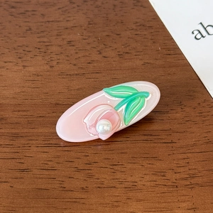 Detailed close-up of a pink tulip hair clip with pearl center on wood surface