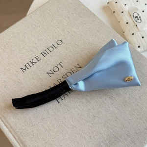 Detail of light blue satin banana hair clip with elegant pleated wings and gold logo