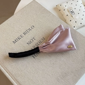 Detailed view of dusty pink satin banana clip with a golden tag on a soft fabric book